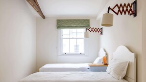 Una camera da letto con due letti, una finestra con tenda verde, una lampada e una testiera in legno.