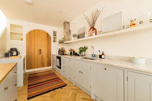 Cozinha moderna com porta de madeira, armários brancos, bancada de mármore e piso em padrão herringbone.