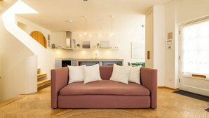 Un soggiorno moderno con un divano rosa, pavimento in legno, una cucina sullo sfondo e una scala a chiocciola.