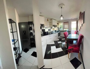 A modern kitchen with a black and white checkered floor, white cabinets, a black refrigerator, and a dining table with red chairs. - 2-bedroom 1-living room apartment in beautiful area with AC near the Belgrade. (Pancevo)