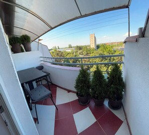 A balcony with a table and chairs, potted plants, and a view of buildings and trees. - 2-bedroom 1-living room apartment in beautiful area with AC near the Belgrade. (Pancevo)