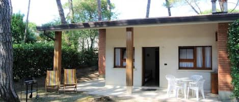A small building with a covered patio, two chairs, and a table.