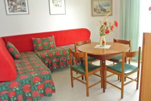 Una habitación con un sofá rojo, una mesa de comedor de madera con sillas y un jarrón con flores.