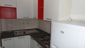 Et køkken med hvide skabe, et rødt skab, en vask og en Beko gasblus.