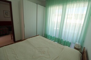 Un dormitorio con cama, armario, mesita de noche y ventana con cortinas ligeras.