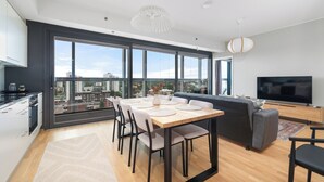 Un espacio habitable moderno con comedor, sofá, TV y ventanas amplias con vista a la ciudad.