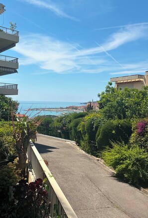 Un chemin pavé bordé de verdure de chaque côté, offrant une vue sur une ville côtière et la mer.