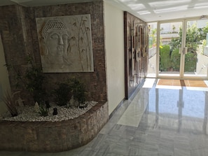 Un intérieur moderne avec un mur en pierre, un grand tableau représentant Bouddha et une porte vitrée donnant sur l’extérieur.