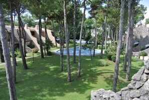 A pool surrounded by tall trees and a stone building. - Cozy villa in a holiday village with pool (Lignano Sabbiadoro)