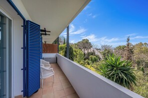 Ein Balkon mit Blick auf einen Garten, ein weißer Stuhl und ein blauer Rollladen.