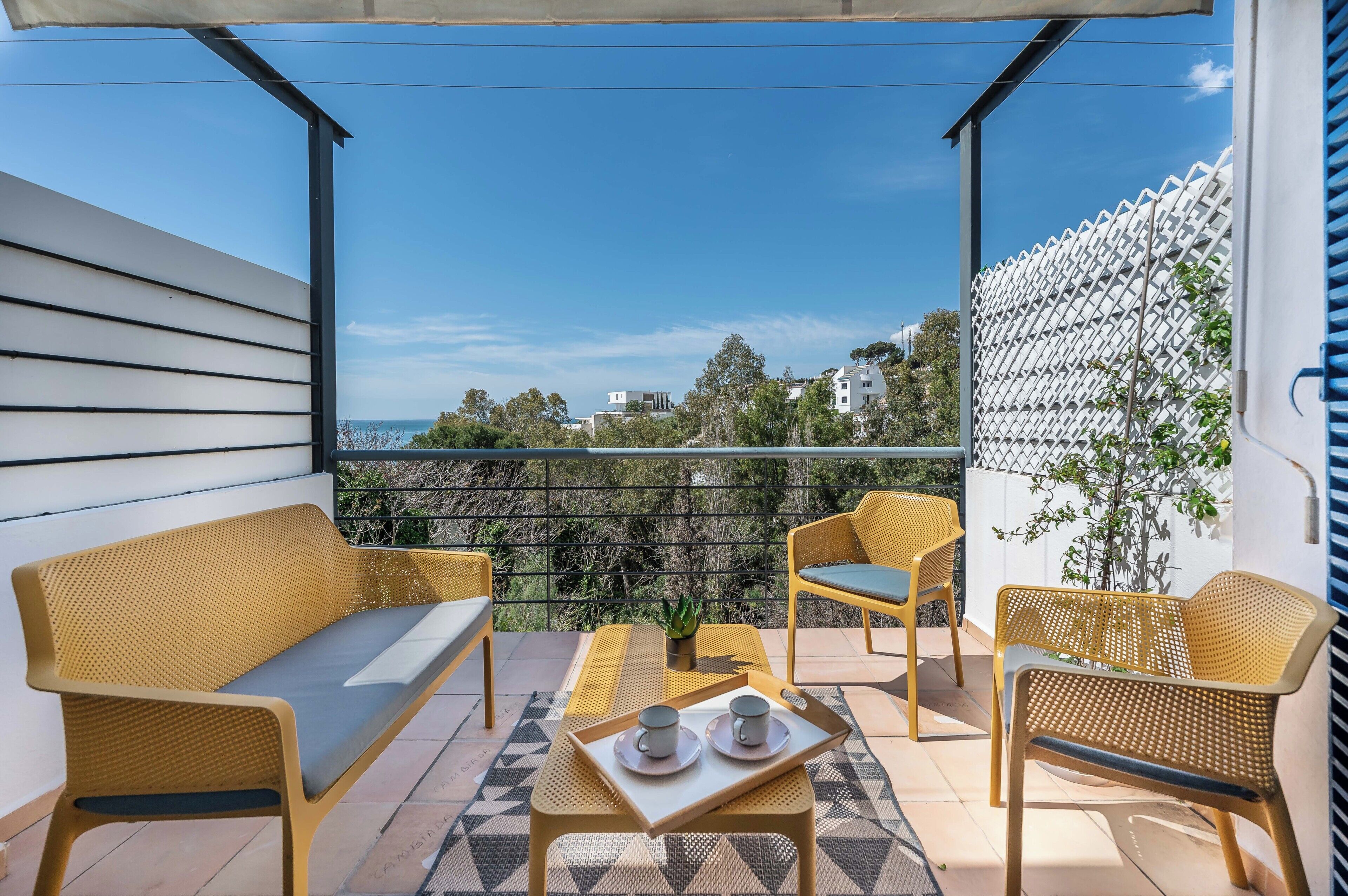 A balcony with wicker furniture, a table with a tray of cups, and a view of the sea.