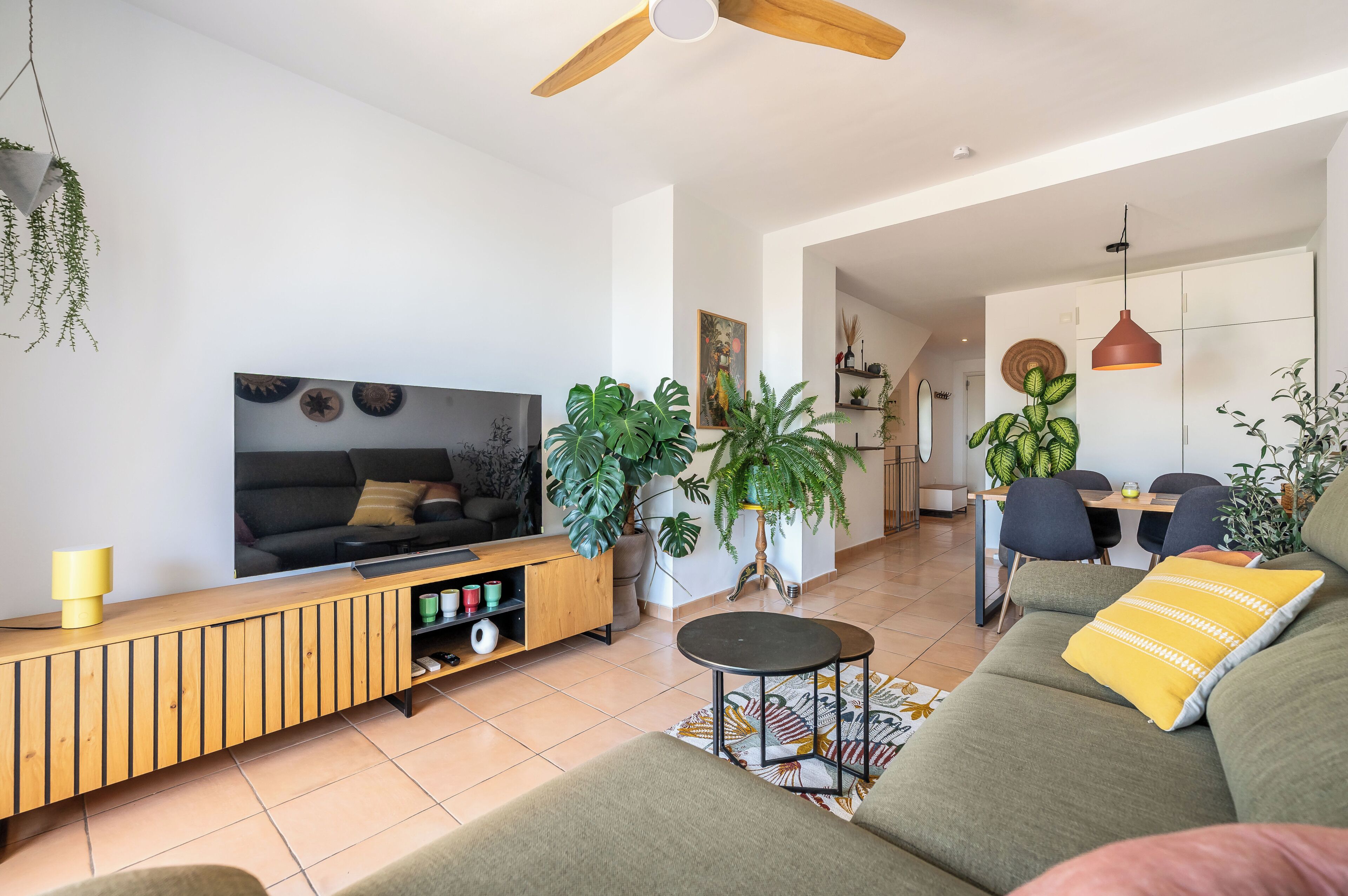 Una sala de estar moderna con sofá, televisor, mueble de madera y plantas en macetas.