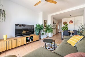 Un salon moderne avec un canapé, un téléviseur, un meuble en bois et des plantes en pot.