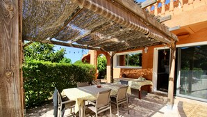 Un patio al aire libre con una mesa, sillas, una pérgola y vistas a un jardín.