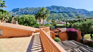 Una terraza con suelo estampado, barandilla y vistas a montañas y casas.