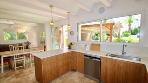 Una cocina con armarios de madera, lavavajillas, fregadero y una zona de comedor con sillas y mesa.