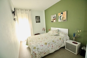 A bedroom with a bed, a nightstand, a dresser, and two wall-mounted pictures.