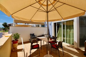 Una terrassa amb taula i cadires, una planta en test i un parasol gran.