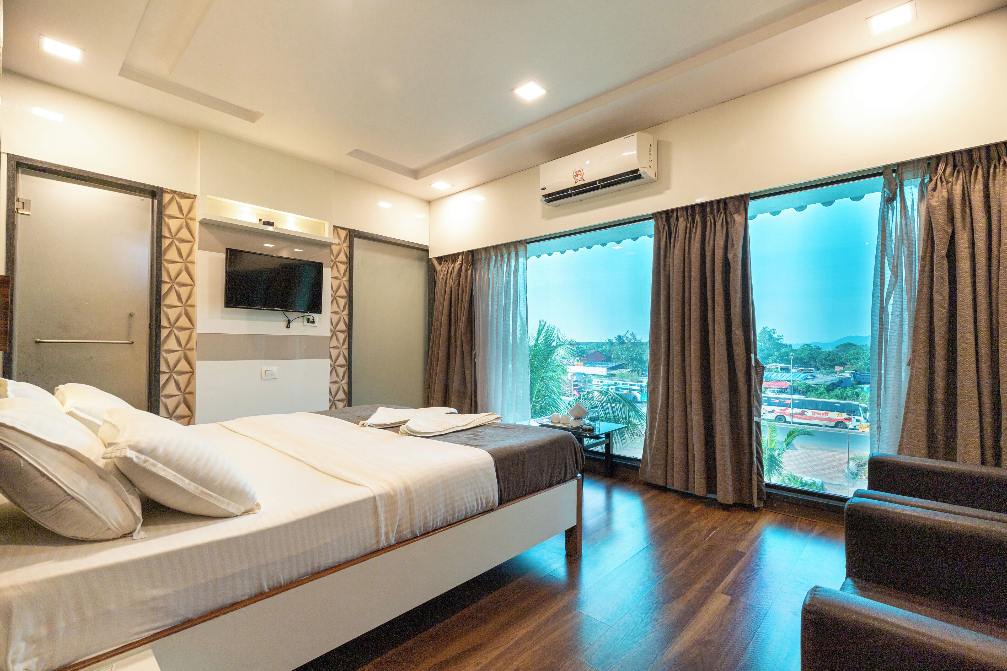 Una habitación de hotel con cama, televisión, escritorio y un ventanal con cortinas.