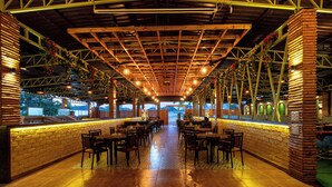 Un restaurante interior con pared de ladrillo, vigas de madera en el techo y lámparas colgantes, con mesas y sillas.