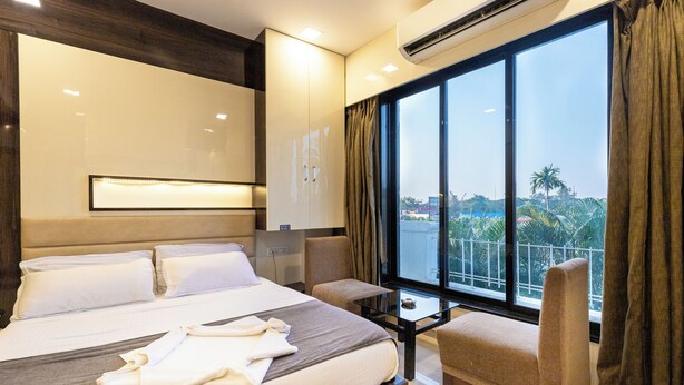 Habitación de hotel con cama, una mesita, una silla y un ventanal con cortinas.