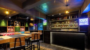 Una zona de bar con una barra larga, taburetes y un letrero de neón.