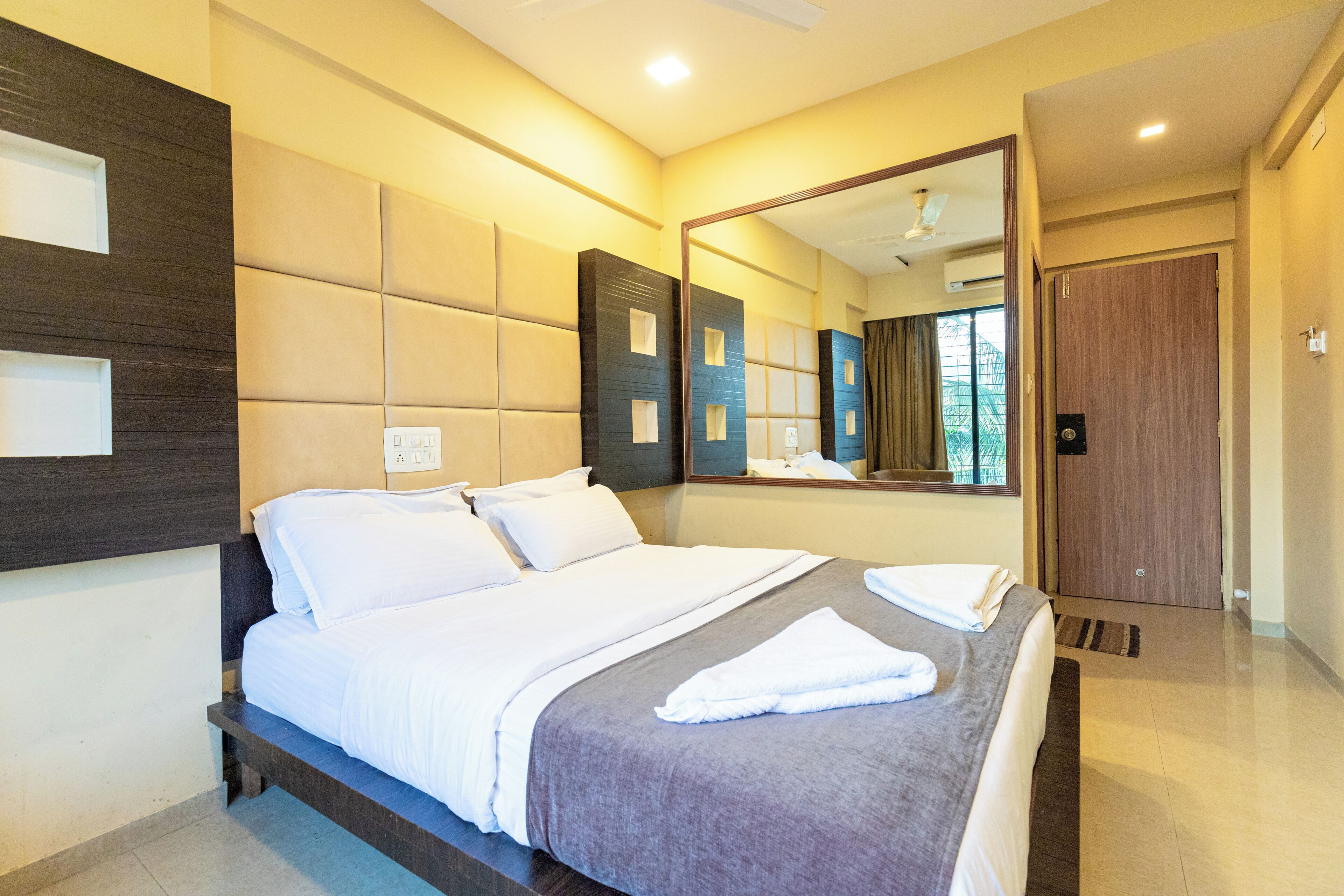 A modern hotel room with a large bed, a mirror, and a door leading to a bathroom.