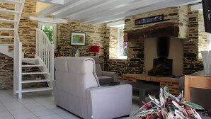 A living room with a stone wall, a sofa, a fireplace, a TV, and a staircase.