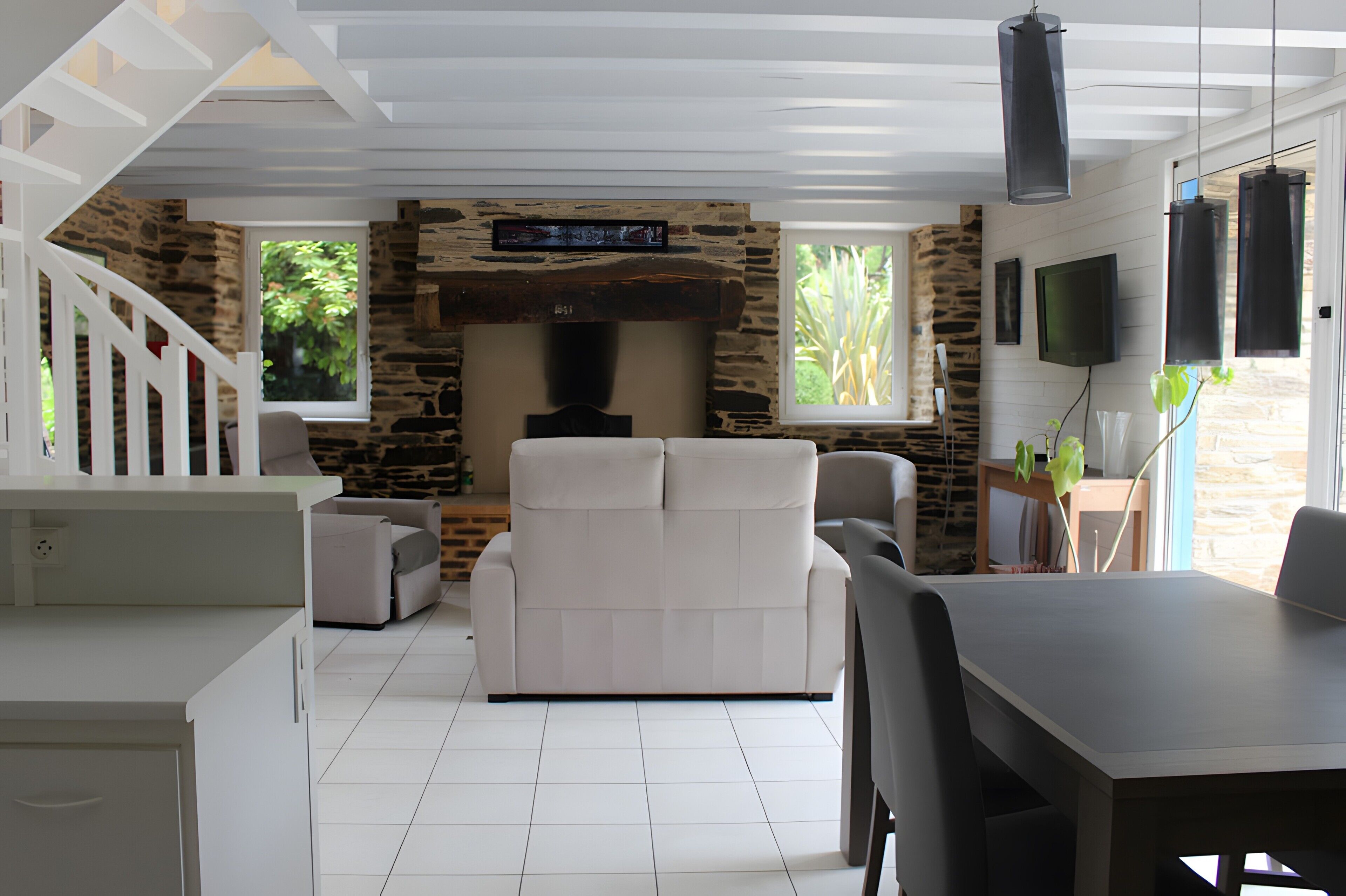 A modern living room with a stone fireplace, white furniture, and a dining area with a table and chairs.
