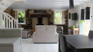 A modern living room with a stone fireplace, white furniture, and a dining area with a table and chairs.
