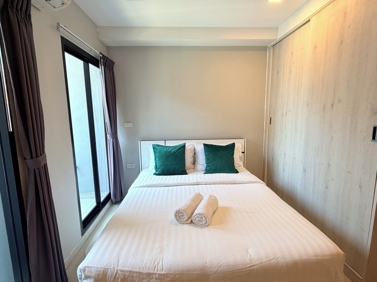 A hotel room with a bed, two pillows, a window with curtains, and a wooden wardrobe.