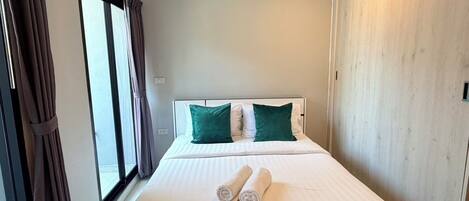 A hotel room with a bed, two pillows, a window with curtains, and a wooden wardrobe.