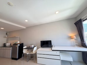 Ein modernes Hotelzimmer mit einer Küchenzeile, einer Essecke, einem Schreibtisch mit Computer und einem großen Fenster mit Vorhängen.