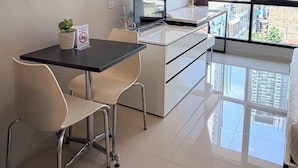A modern hotel room with a dining area, a TV, a lamp, and a view of the cityscape. - LKN Grand Ratchathewi (Bangkok)