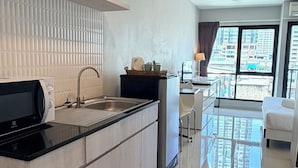 A modern kitchen with a black countertop, stainless steel appliances, and a view of the city through large windows. - LKN Grand Ratchathewi (Bangkok)
