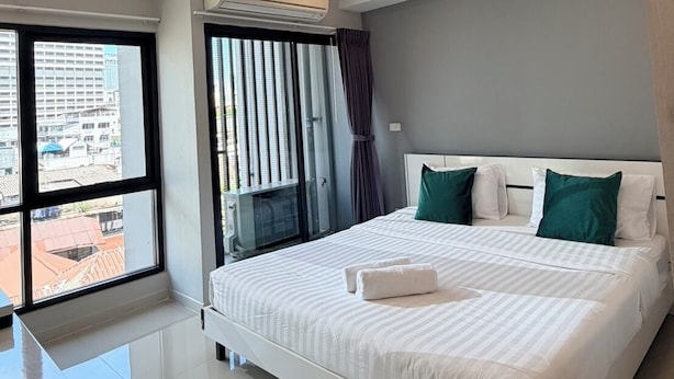 A modern hotel room with a large bed, a window with a view of buildings, an air conditioning unit, and a ceiling light. - LKN Grand Ratchathewi (Bangkok)
