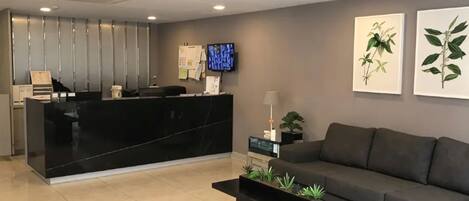 A reception area with a black marble counter, a grey sofa, a coffee table with plants, and two framed botanical prints on the wall.