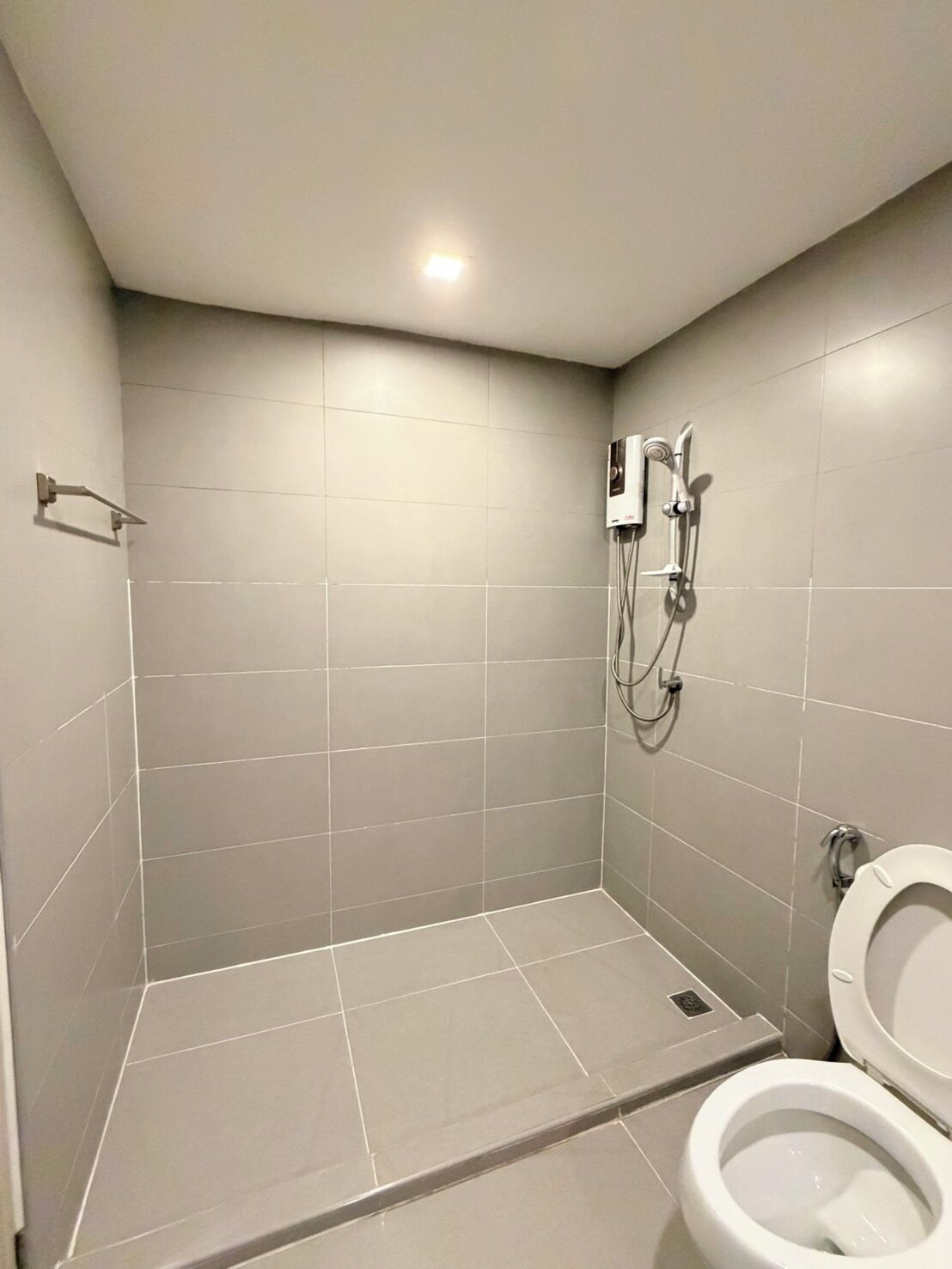 A small, modern bathroom with a shower, toilet, and a wall-mounted water heater.