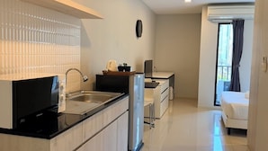 A modern kitchen with a microwave, refrigerator, and sink. There is a dining area with a table and chairs. The room has a large window with curtains. - LKN Grand Ratchathewi (Bangkok)