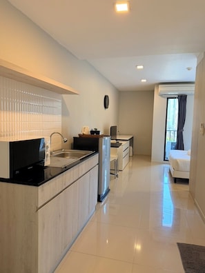 Uma cozinha moderna com micro-ondas, frigorífico e pia. Possui uma área de refeições com mesa e cadeiras. O quarto tem uma janela grande com cortinas.