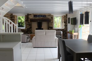 Uma sala de estar moderna com lareira de pedra, mobiliário branco e uma área de jantar com mesa e cadeiras.