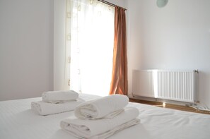 A hotel room with a bed, rolled white towels, a window with curtains, and a radiator. - Alexys Residence 4 cozy apartment in welcoming Iași with AC (Iași)