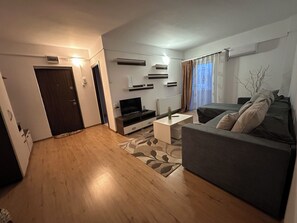Un soggiorno moderno con divano, tavolino, televisore e una porta che dà su un'altra stanza.
