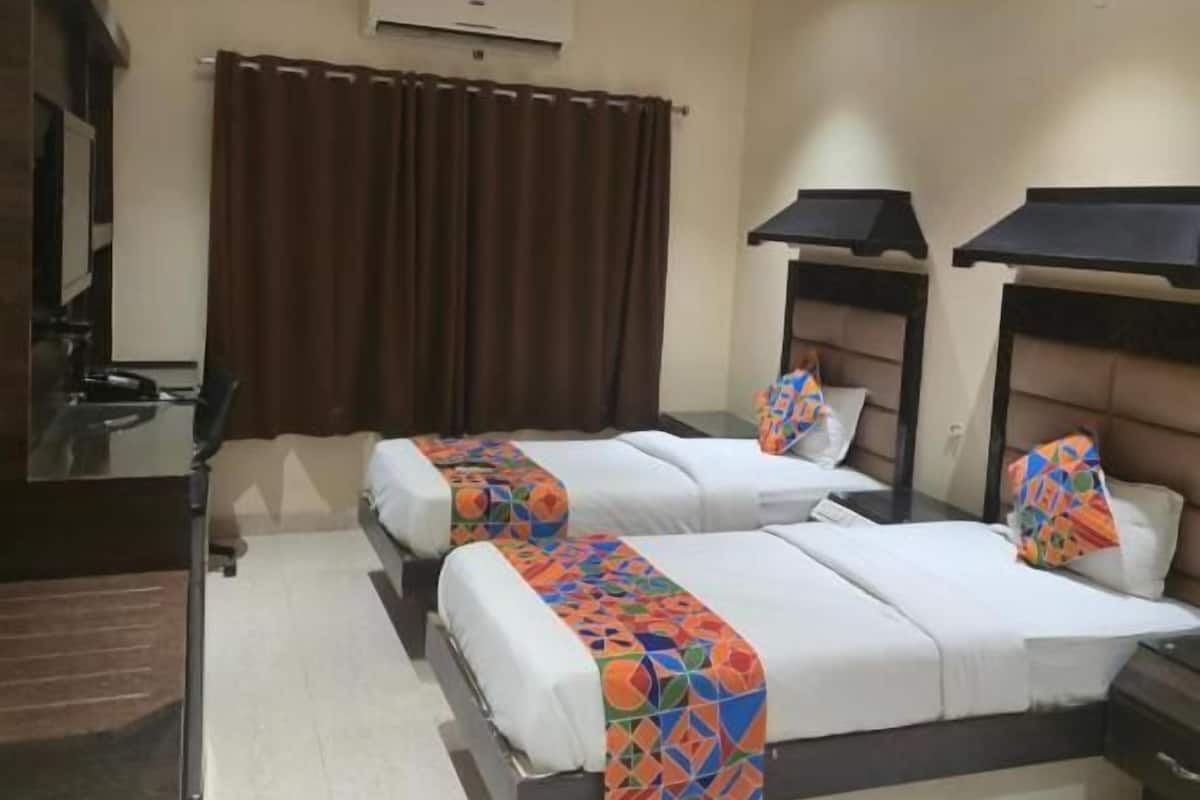A hotel room with two beds, a desk, an air conditioning unit, and a ceiling fan.