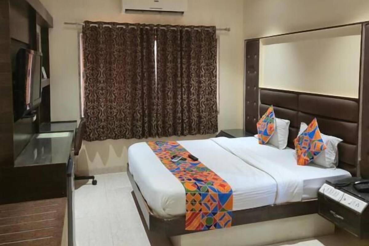 A hotel room with a bed, a desk, a chair, a TV, a ceiling fan, and curtains.