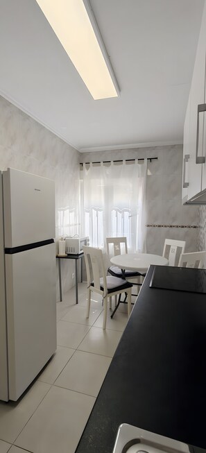 A modern kitchen with a refrigerator, a dining table with chairs, and a black countertop. - Apartment in A Hotel 'Las Calas A' with Shared Pool, Wi-Fi and Air Conditioning (Torrevieja)