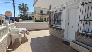 A residential area with a white house, a gated entrance, a table with chairs, and a stop sign.