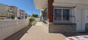 A narrow street with a house on the right, featuring a stone wall, a metal gate, and a door with a window. - Apartment in A Hotel 'Las Calas A' with Shared Pool, Wi-Fi and Air Conditioning (Torrevieja)