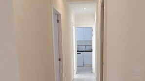 A hallway with white walls and tiled flooring leading to a kitchen area.