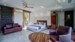 Un dormitorio moderno con cama, sofá, sillón, una mesa redonda de madera y ventilador de techo.